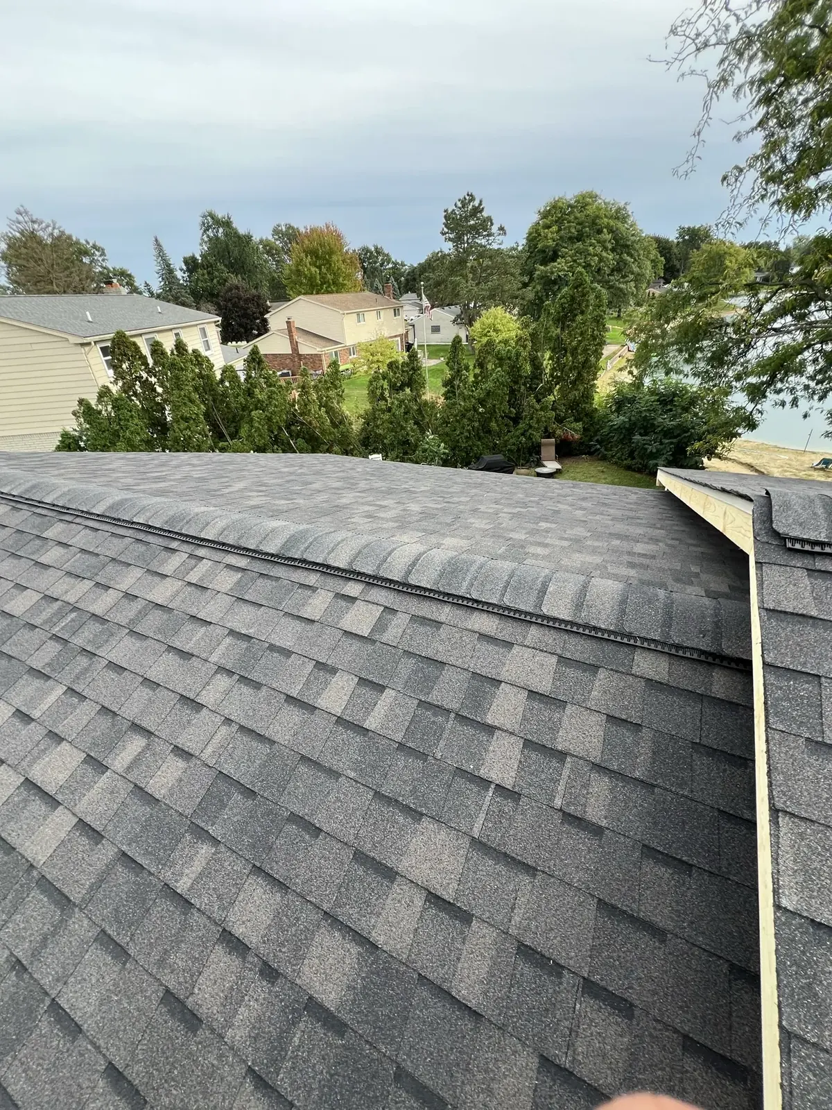 A finished gray shingle roof with a straight ridge cap line, trees and neighboring homes beyond