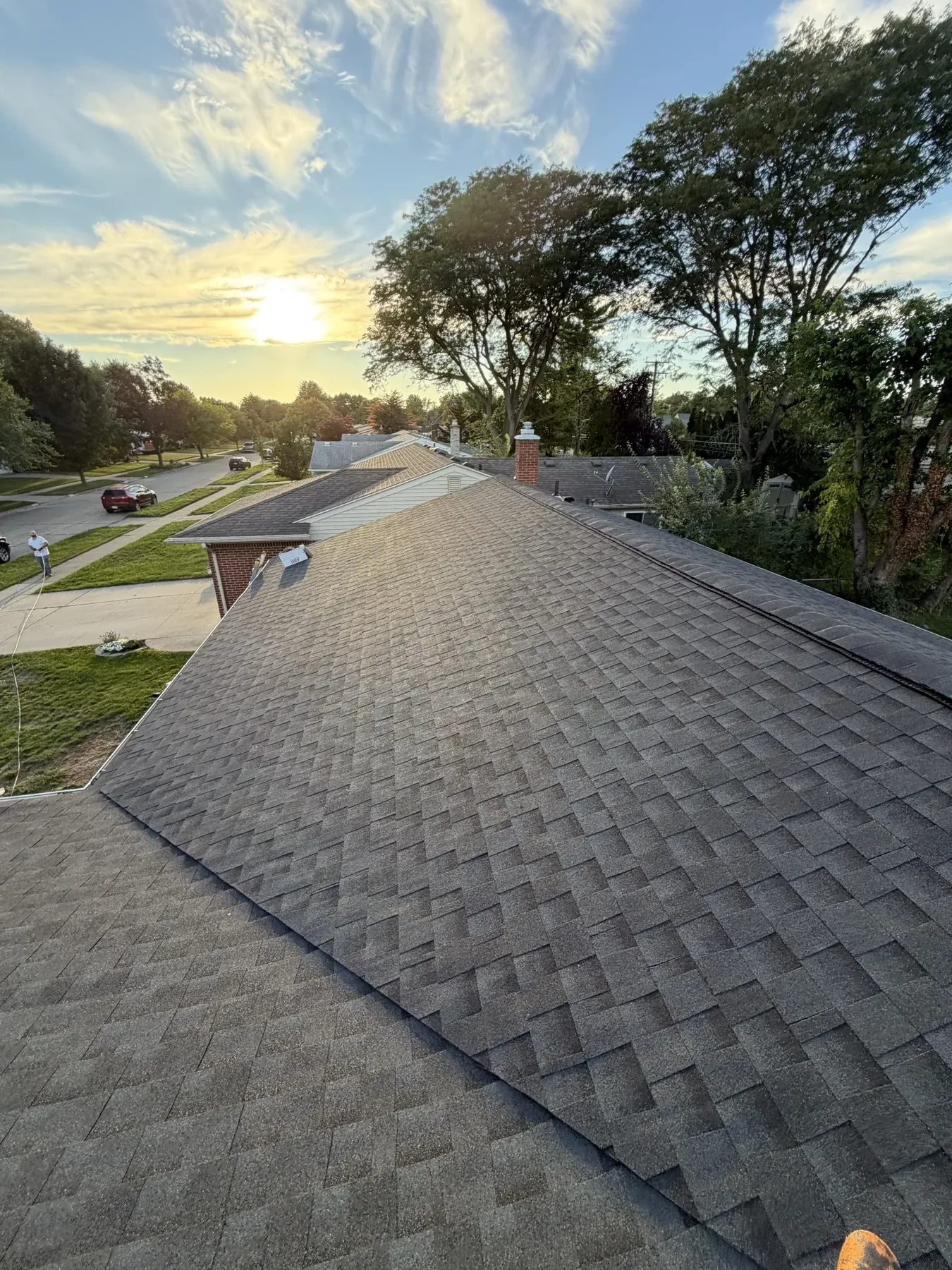 A finished DripRite gray shingle roof at golden hour above a tree-lined street