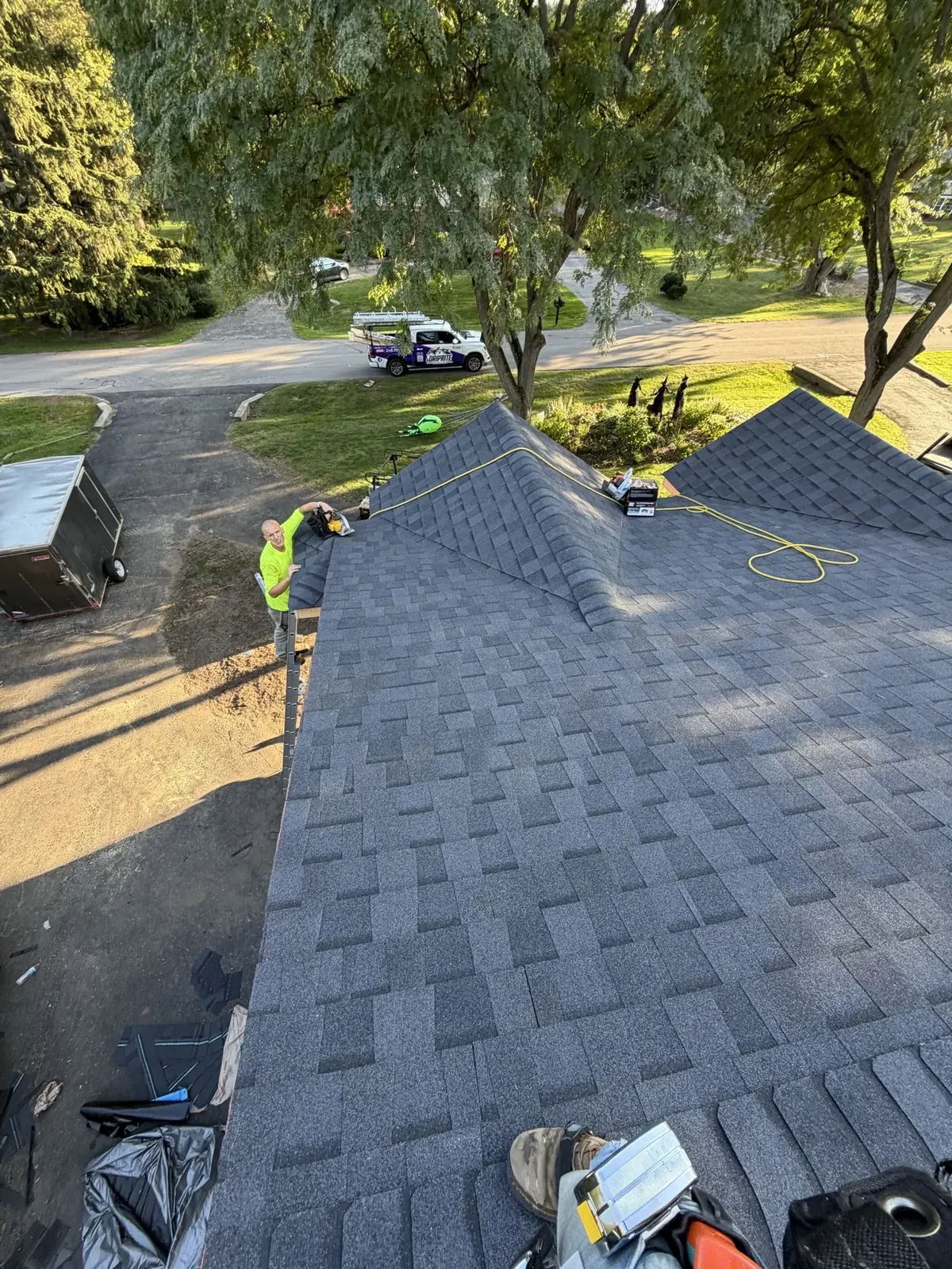Looking down a new gray shingle roof during installation, with the crew and equipment below