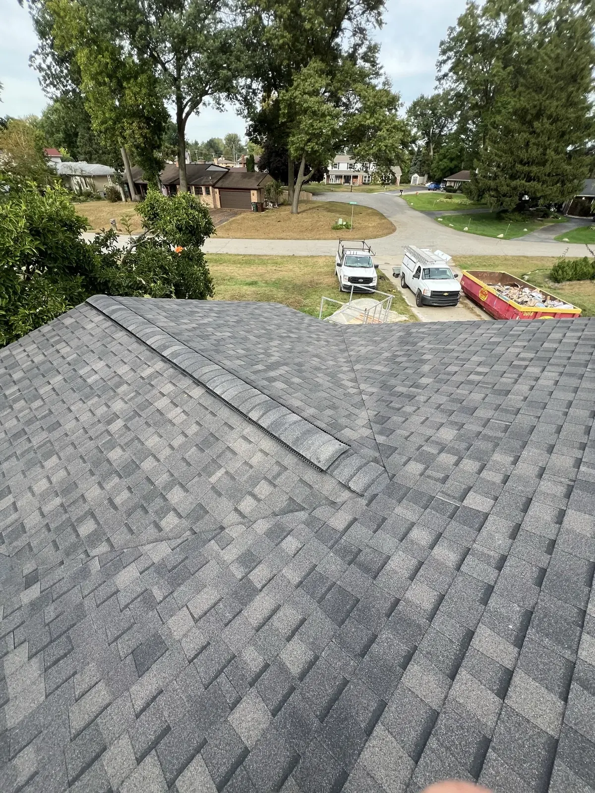 Two slopes of a new gray shingle roof meeting at a valley, with work trucks on the street below